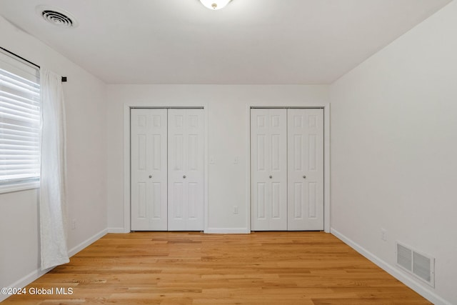 unfurnished bedroom featuring light wood-type flooring and two closets