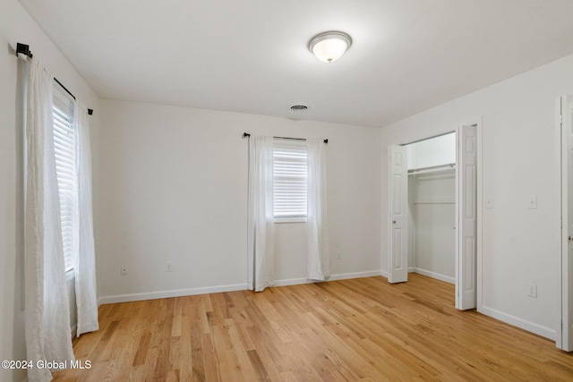 unfurnished bedroom featuring multiple windows, a closet, and light hardwood / wood-style floors