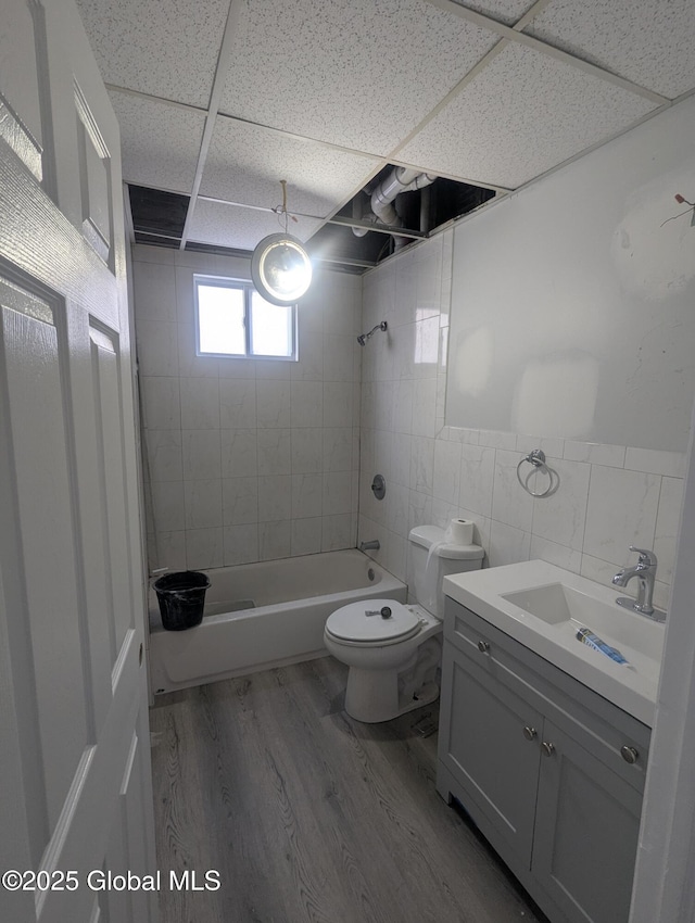 full bathroom featuring tiled shower / bath, hardwood / wood-style floors, tile walls, vanity, and toilet