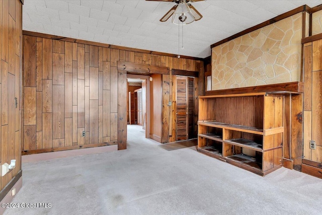 unfurnished living room featuring light carpet, ceiling fan, and wood walls