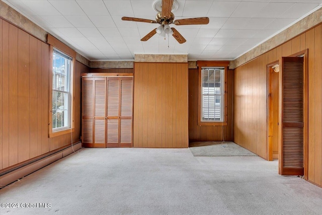 unfurnished bedroom featuring multiple closets, ceiling fan, a baseboard heating unit, wood walls, and light carpet