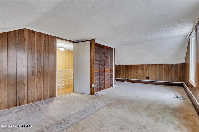 spare room featuring vaulted ceiling, wood walls, light carpet, and a textured ceiling