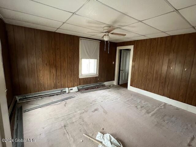 unfurnished room with a drop ceiling, wood walls, and ceiling fan