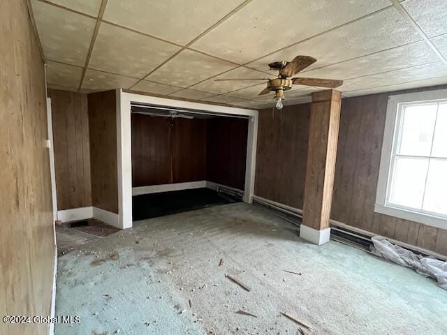 interior space featuring a paneled ceiling, ceiling fan, and wood walls