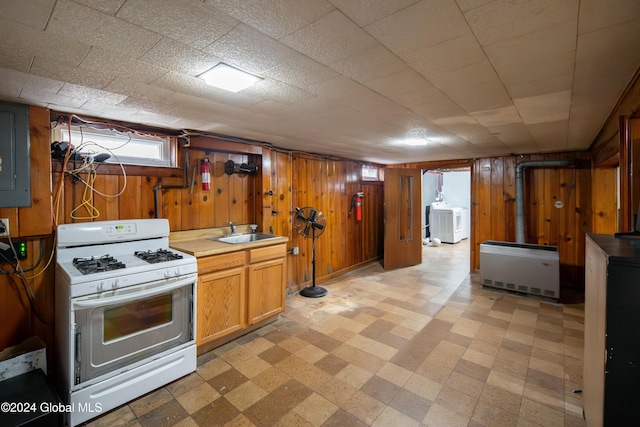 kitchen with wood walls, washer / dryer, white gas range, and sink