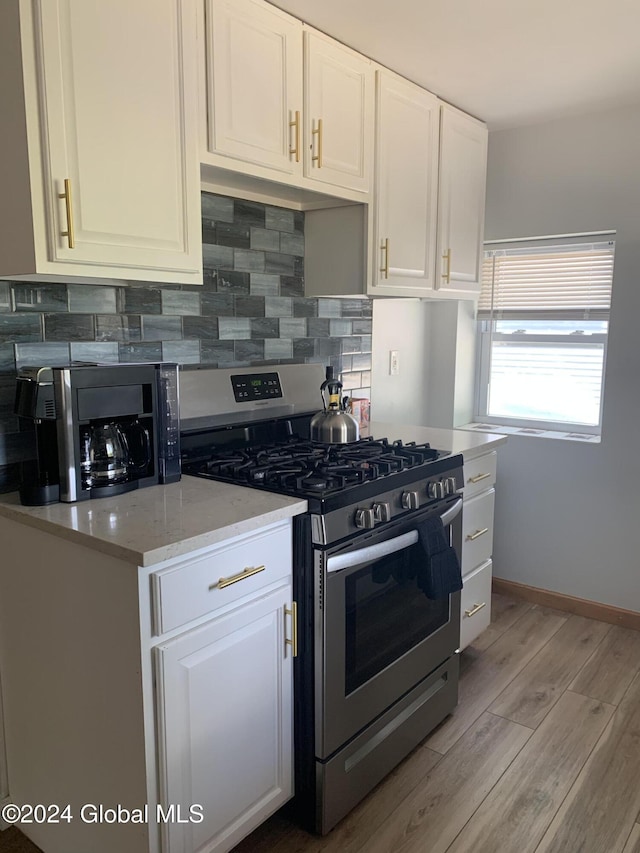 kitchen featuring backsplash, light stone counters, stainless steel gas range oven, light hardwood / wood-style floors, and white cabinets