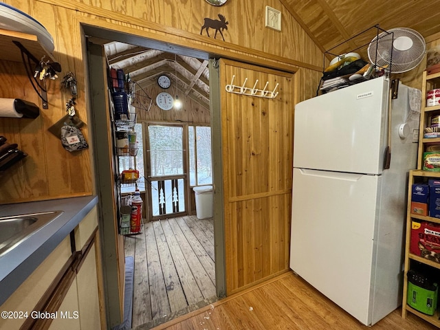 kitchen with wood walls, white refrigerator, lofted ceiling, and light hardwood / wood-style floors