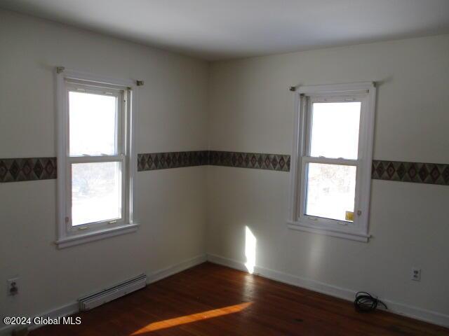 unfurnished room with plenty of natural light, dark wood-type flooring, and a baseboard heating unit