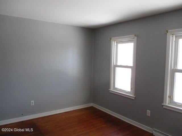 unfurnished room with a healthy amount of sunlight, dark hardwood / wood-style flooring, and baseboard heating