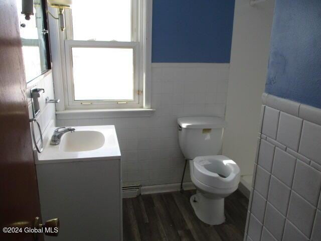 bathroom with vanity, a baseboard heating unit, hardwood / wood-style flooring, toilet, and tile walls