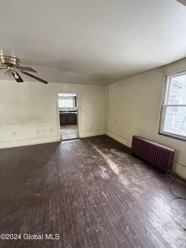 spare room with radiator heating unit, a wealth of natural light, and dark wood-type flooring