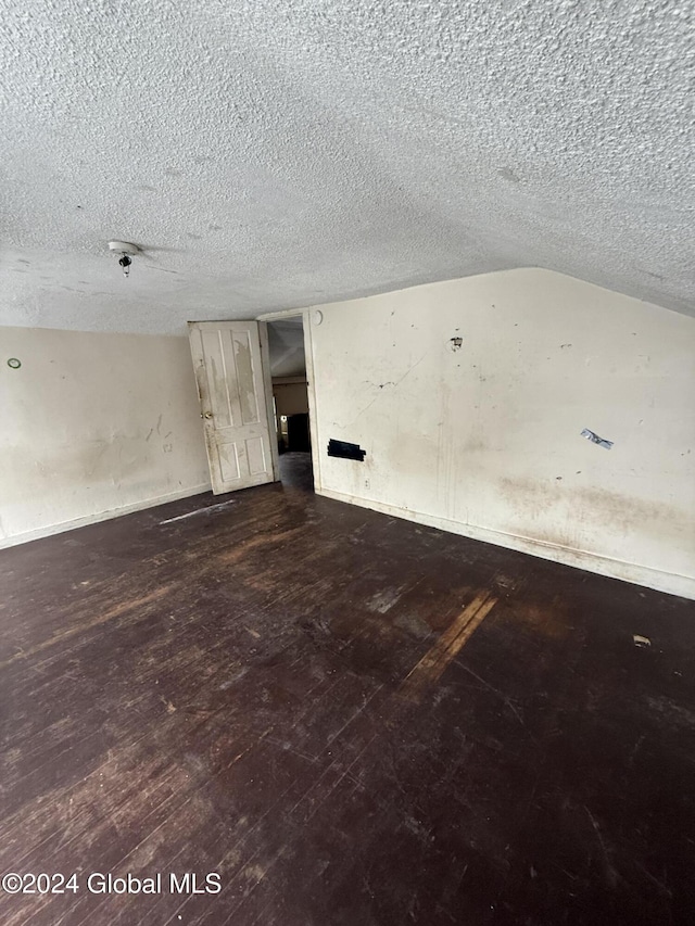 empty room with lofted ceiling, dark hardwood / wood-style flooring, and a textured ceiling