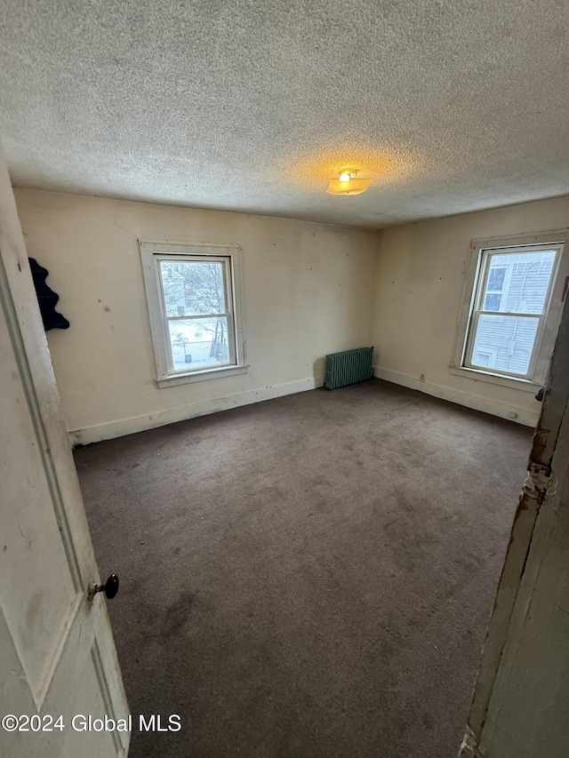 carpeted spare room featuring a healthy amount of sunlight, radiator heating unit, and a textured ceiling