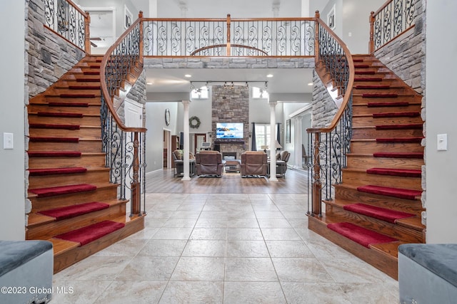 foyer featuring a towering ceiling, ornate columns, and a stone fireplace