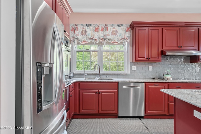 kitchen featuring decorative backsplash, appliances with stainless steel finishes, light stone counters, and sink