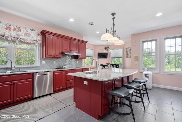 kitchen featuring stainless steel dishwasher, light stone counters, sink, and an island with sink