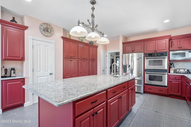 kitchen with sink, stainless steel appliances, dark tile patterned floors, an island with sink, and decorative light fixtures