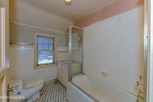 bathroom featuring combined bath / shower with glass door, toilet, and tile walls