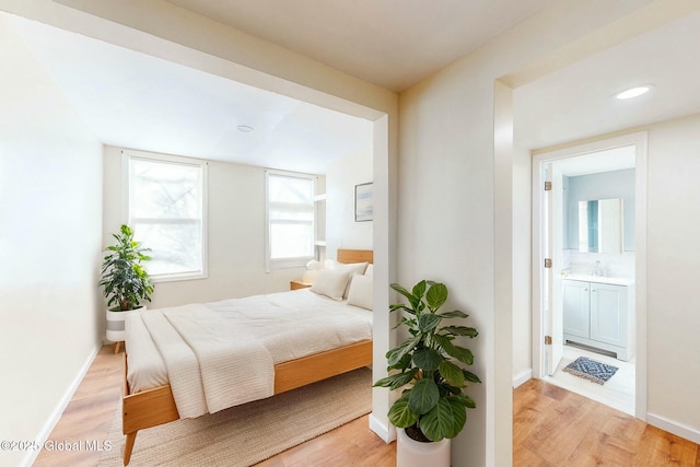 bedroom featuring baseboards, recessed lighting, ensuite bathroom, light wood-style floors, and a sink