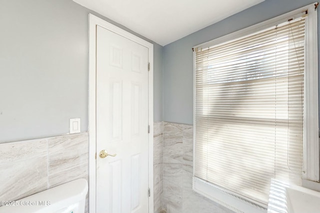 bathroom featuring toilet, tile walls, and wainscoting