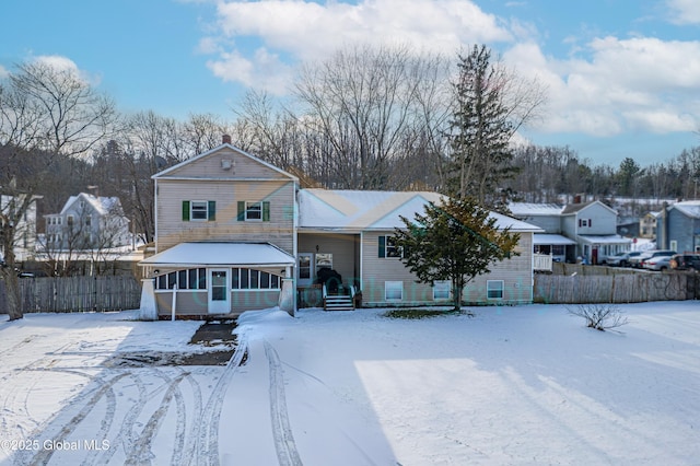 snow covered back of property featuring a sunroom