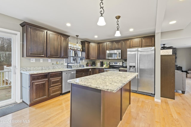 kitchen featuring dark brown cabinetry, a center island, stainless steel appliances, decorative light fixtures, and light wood-type flooring