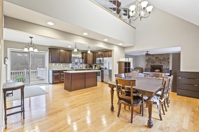 dining area with a high ceiling, ceiling fan with notable chandelier, light hardwood / wood-style flooring, and a stone fireplace