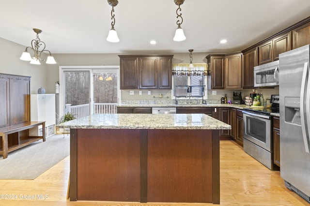 kitchen with light wood-type flooring, appliances with stainless steel finishes, a center island, and decorative light fixtures