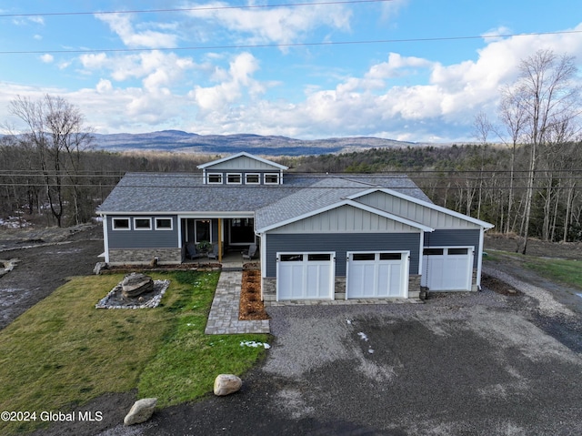 view of front of home featuring stone siding, a mountain view, gravel driveway, a front yard, and a shingled roof