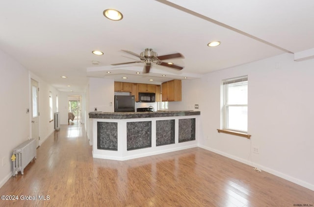 kitchen featuring black appliances, light hardwood / wood-style floors, kitchen peninsula, and radiator