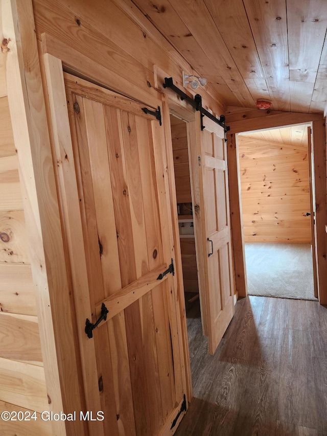 hall with a barn door, wood ceiling, dark wood-type flooring, and wooden walls