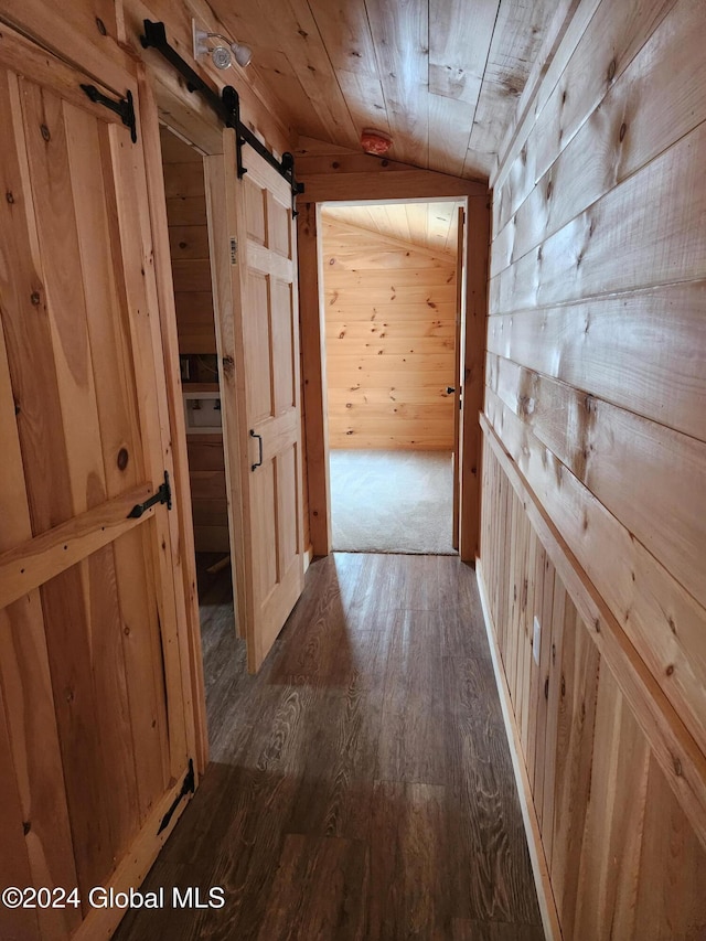 corridor with wood walls, wooden ceiling, vaulted ceiling, a barn door, and dark hardwood / wood-style flooring