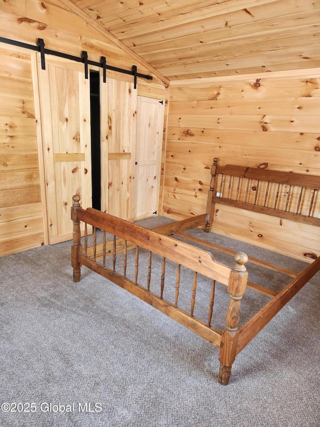 unfurnished bedroom featuring a barn door, wood walls, carpet floors, and vaulted ceiling