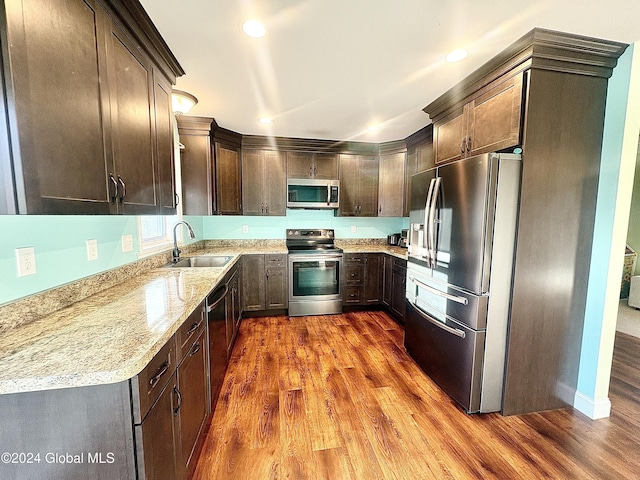 kitchen featuring dark brown cabinetry, light stone countertops, sink, dark hardwood / wood-style flooring, and appliances with stainless steel finishes