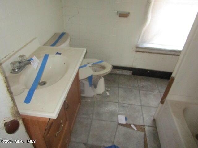 bathroom with vanity, a tub to relax in, toilet, and tile walls