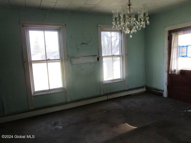 unfurnished dining area with concrete floors, an inviting chandelier, and a baseboard heating unit