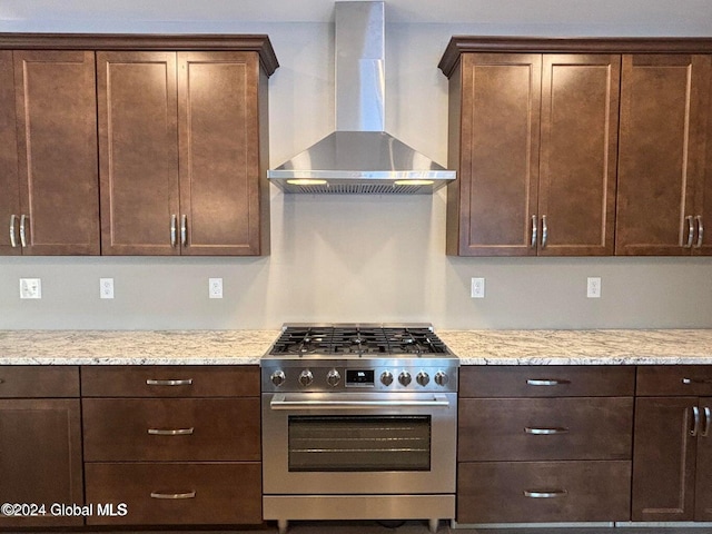 kitchen with wall chimney exhaust hood, dark brown cabinets, light stone countertops, and stainless steel range