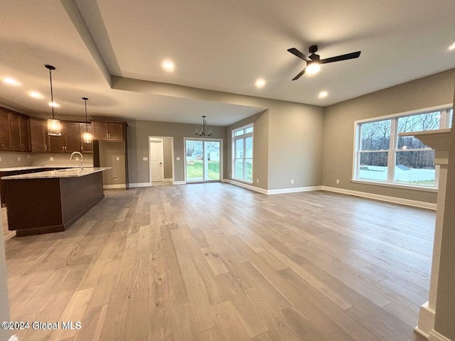 unfurnished living room with ceiling fan with notable chandelier, sink, and light hardwood / wood-style flooring