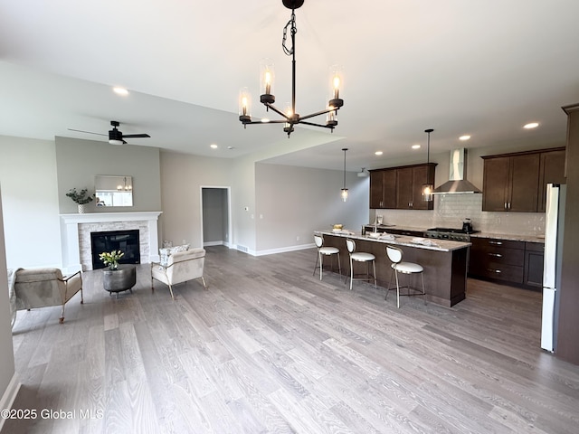 13 Bernie Loop, North Greenbush, NY 12180 - kitchen with wall chimney exhaust hood, dark brown cabinetry, a breakfast bar, light wood finished floors, and baseboards