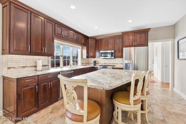 kitchen featuring backsplash, a kitchen breakfast bar, light stone countertops, a kitchen island, and stainless steel appliances