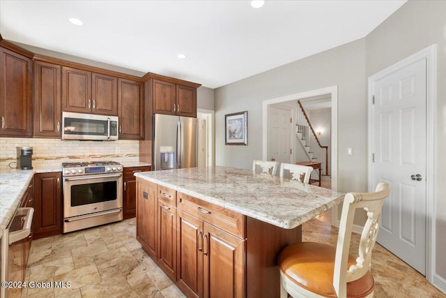 kitchen featuring light stone countertops, a center island, a kitchen breakfast bar, backsplash, and appliances with stainless steel finishes