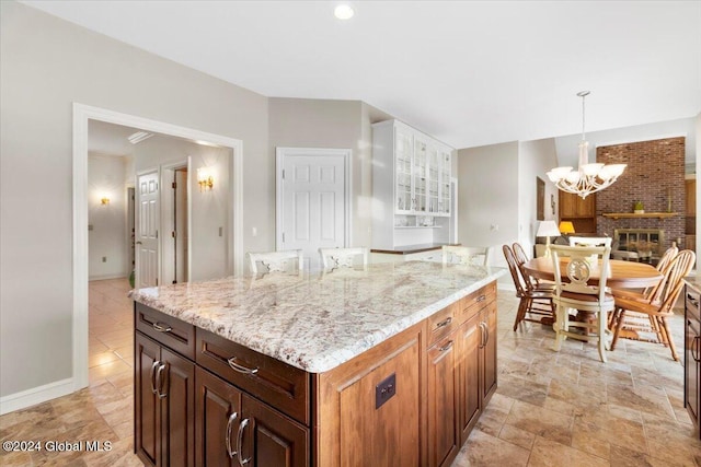 kitchen with a center island, light stone countertops, a fireplace, decorative light fixtures, and a chandelier