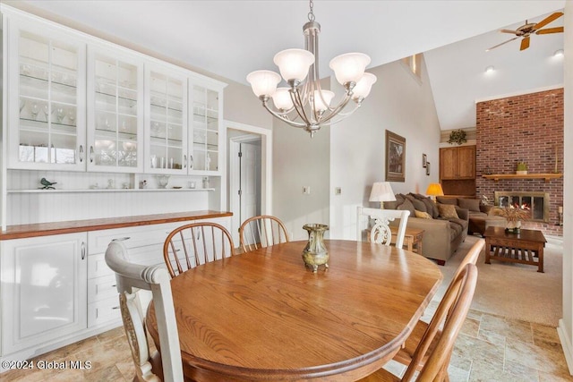 dining area with high vaulted ceiling, ceiling fan with notable chandelier, and a brick fireplace