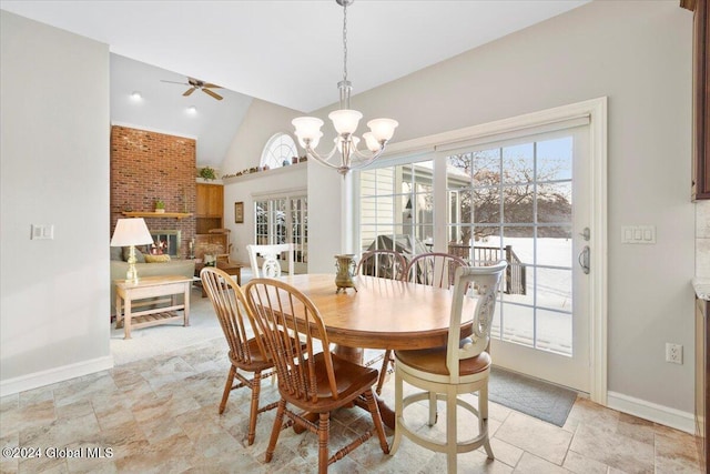 dining room with plenty of natural light, a fireplace, ceiling fan with notable chandelier, and vaulted ceiling