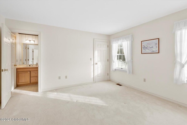 unfurnished bedroom featuring light carpet and ensuite bath