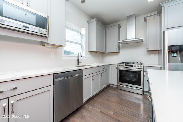 kitchen featuring appliances with stainless steel finishes, sink, wall chimney range hood, pendant lighting, and dark hardwood / wood-style floors