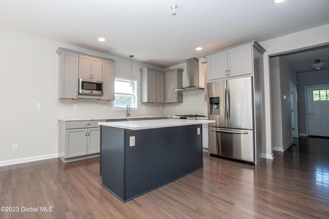 kitchen featuring dark wood-type flooring, wall chimney exhaust hood, gray cabinets, decorative light fixtures, and stainless steel appliances