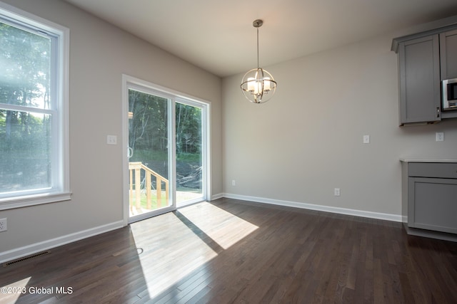 unfurnished dining area featuring a wealth of natural light, dark hardwood / wood-style flooring, and a chandelier