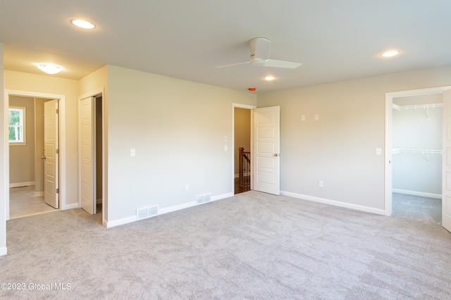 unfurnished bedroom with ceiling fan, light colored carpet, a spacious closet, and a closet