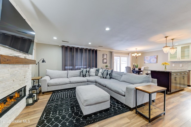 living room with crown molding, an inviting chandelier, light hardwood / wood-style flooring, and a stone fireplace